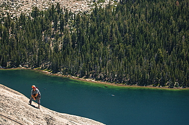 View of single adventurous man rock climbing above lake in?Tuolumne?Meadows, Yosemite National Park, California, USA