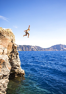 View of man in mid-air while cliff jumping into Crater Lake, Oregon, USA