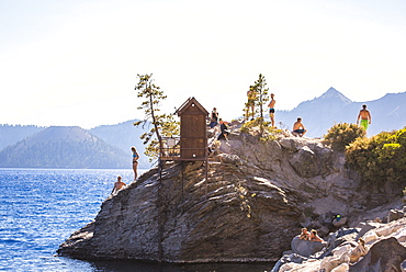 Swimmers wait on a rock outcrop surrounded by a big blue lake on sunny summer day, Crater Lake, Oregon, USA