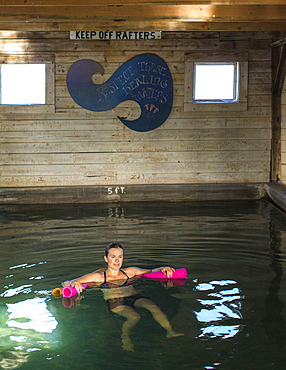 Single mid adult woman swimming in indoor hot spring inside barn, Summer Lake, Oregon, USA