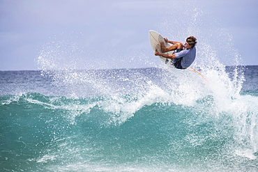 A male surfer gets air and grabs the edge of his board off the lip of a wave on the north shore of Oahu, Hawaii