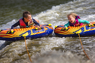 Front view of two children having fun tubing on river