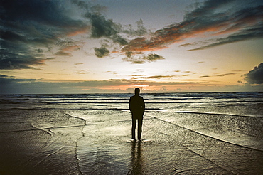 A man stands on the beach watching the waves and sunset over the Pacific Ocean, Oregon, USA