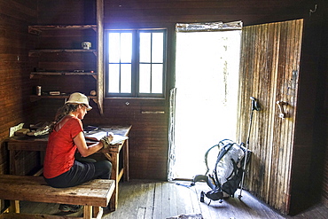 A thru hiker takes a break at Theodore Roosevelts Cabin on the Muav Saddle, far out on the North Rim of the Grand Canyon, and signs a storied trail register, Arizona, USA