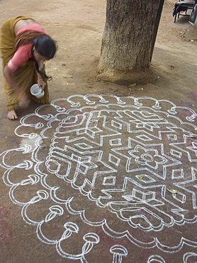 A woman performs the morning ritual of making a Rangoli, a Hindu religious decoration, outside her home in Hampi, Karnataka, India.