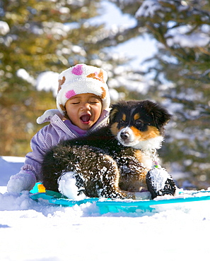 1-year-old baby girl sledding with her dog, a 12-week-old puppy, in Carbondale, Colorado.