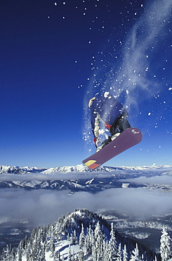 Young male snowboarder (Steve Whelan) in the air over cloud-shrouded valley at Fernie Alpine Resort, Fernie, British Columbia, Canada.