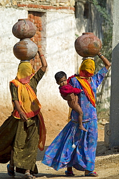 A Rajasthani woman with a burqua (veil) covering her face walks toard the village well with her young son on her hip. In Rajasthani tradition she carries her ceramic water pot balanced on her head.