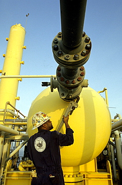 A oil drilling worker holds a large wrench and tightens a knob.