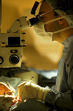 A surgeon works on a patient while looking through a microscope for exact detail.