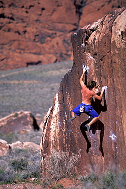 Male rock climber Adam Stack crimping and hanging out while climbing on a bouldering route in Red Rocks Conservation Area outside of Las Vegas, Nevada.