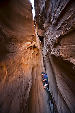 A man chimneying down a slot canyon, Utah.