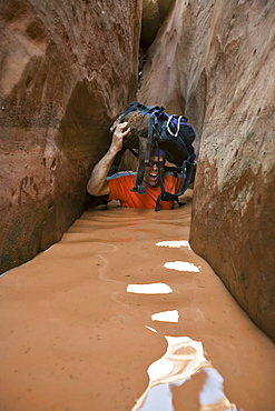 A man wading through water in narrow canyon, Utah.