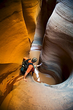 A man descending into water in sculpted slot canyon, Utah.