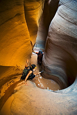 A woman down climbing into pool with man in pool in sculpted slot canyon, Utah.