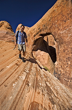 A man hiking next to a sandstone arch, Moab, Utah.