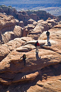 Three hikers approaching a view, Arches National Park, Moab, Utah.