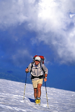 Climber in shorts with trekking poles summits Mount Rainier, Washington.