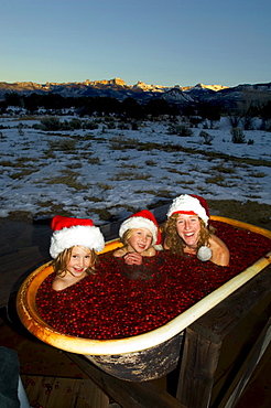 Woman and her daughters with Santa Hats sitting in a cranberry filled bathtub outdoors, San Juan Mountains, Cimmaron Ridgw, Ridg