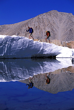 Two hikers on a glacier reflecting in a lake in Eastern Sierra Nevada mountains, California.