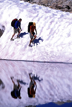 Two hikers on a glacier reflecting in a lake in Eastern Sierra Nevada mountains, California.