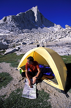 Man looking at his map beside his tent in Eastern Sierra Nevada mountains, California.