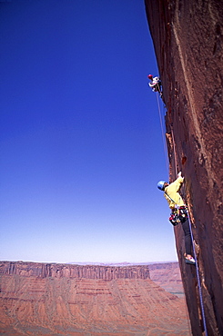 Two rock climbers scale a vertical sandstone cliff in Castle Valley, Utah.