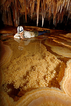 A female cave explorer looks into a very pretty Gour Pool. The floor of which is covered with 'dog tooth' crystals. The edges of