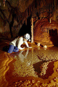 A female cave explorer looks into a crystal clear Gour Pool surrounded by delicate Stalactite formations.