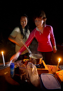 Two female cave explorers prepare an evening meal under candle light, deep inside Whiterock (cave).