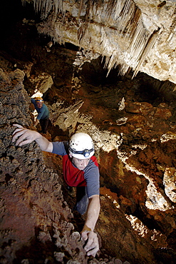 Two cave explorers traverse a section of cave on a ledge above a deep hole.