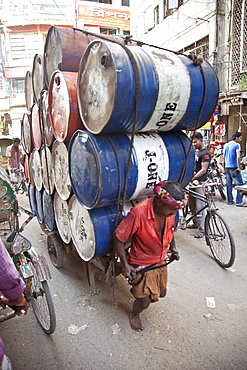 Dhaka,  Bangladesh - July 2011: Busy street  in Dhaka,  Bangladesh with a man pulling a wagon loaded high with 20 oil drums.