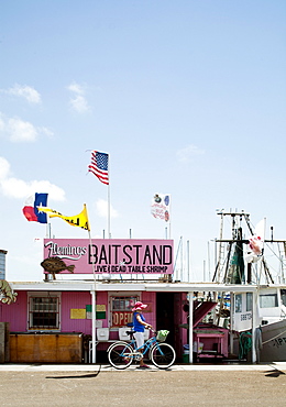 ROCKPORT, TEXAS, USA. A woman walks her bike in front of a bait stand in a small coastal town.