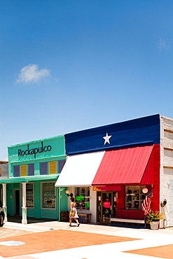 ROCKPORT, TEXAS, USA. A woman walks in front of a store front on a sunny day.