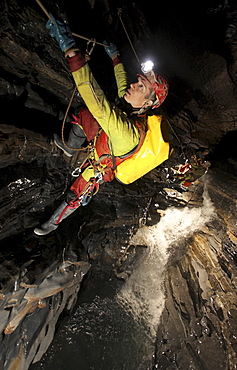 A young man holds onto a rope above a river in a cave in China.