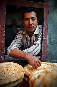 Young Uyghur man selling bread in a window of a traditional Uighur bakery in Kashgar, Xinjiang, China.