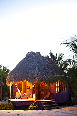 A woman sits in a hammock on the porch of her thatch cabana at a luxury hotel in Belize.