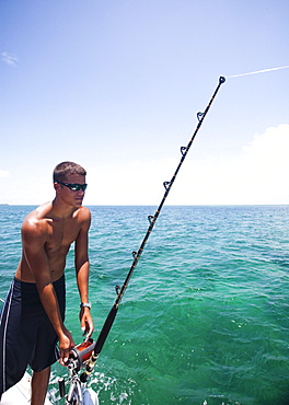 A young man lets fishing line out of his reel while deep sea fishing in Belize.