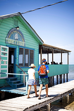 A couple walk down a dock near a ocean side restaurant.