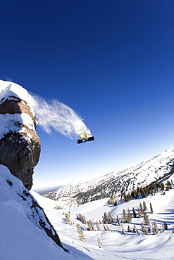 A male snowboarder jumps off a large cliff in the Grand Targhee ski area backcountry, Wyoming.