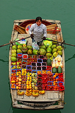 fruit seller paddles boxes of fruit in a boat on Halong Bay.