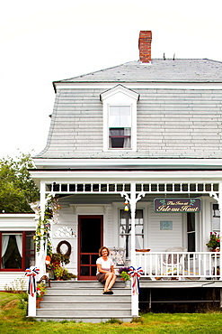 A innkeeper sits on the porch of her bed & breakfast.