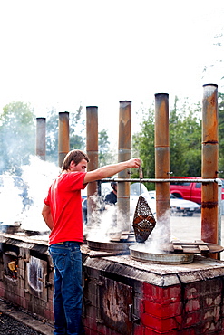 A man lifts a bag of cooked lobsters out of an outdoor oven at a restaurant.