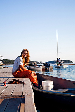 A portrait of a young woman sitting on the edge of a dock with her feet in the boat.