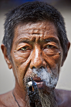 Portrait of an Indonesian man smoking a cigerette with a pair of plyers in Sukadana, Indonesian Borneo.