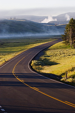 A road winds through the grasses of Hayden Valley in Yellowstone National Park, Wyoming on July 24, 2005 as mist rises in the background.