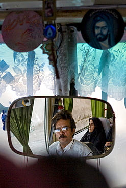 Dasht e Kavir, Iran - February, 2008: Bus driver and female passenger dressed in black reflected in the mirror of a bus enroute through the desert from Esfahan to Khur in Central Iran.