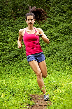 Woman trail running through a green meadow in the woods.