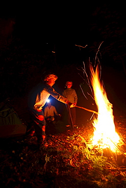 Two boys roast marshmallows over a campfire.