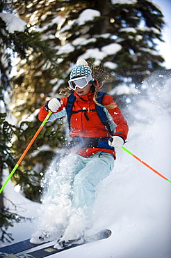 A woman backcountry skier catches air in the trees of the Selkirk Mountains, Canada.